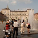 Auf einem Platz vor einem Stadtschloss in Turin stehen Menschen an einer kleinen Fontäne