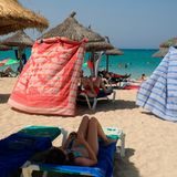 Unter Sonnenschirmen aus Stroh suchen Strandbesucher auf Mallorca Schutz vor der brennenden Sonne