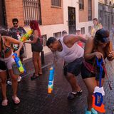 Mit großen, bunten Wasserpistolen bespritzen sich Erwachsene in sommerlicher Kleidung