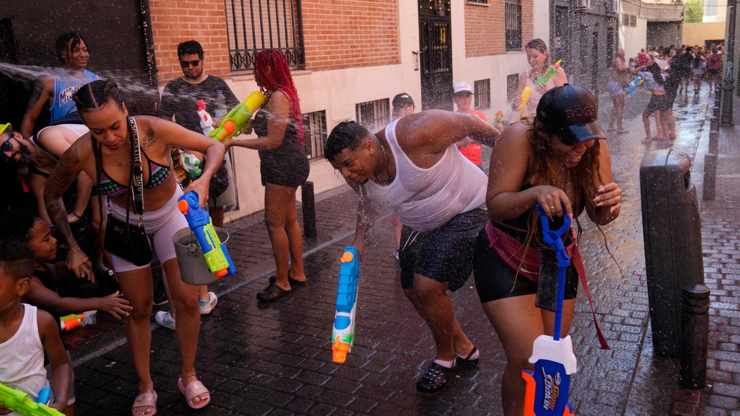 Mit großen, bunten Wasserpistolen bespritzen sich Erwachsene in sommerlicher Kleidung