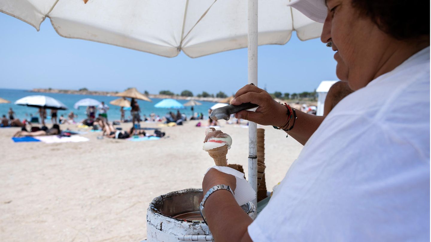 Ein Eisverkäufer steht am Strand eines Athener Vorortes und löffelt gerade eine Kugel Eis in ein Waffelhörnchen