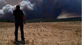 Ein Mann steht auf einem Feld in Inoi und betrachtet den Rauch eines Feuers in der Nähe von Athen. Den dritten Tag in Folge kämpfen Feuerwehrleute in Griechenland gegen drei große Feuerfronten an