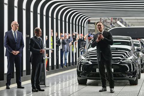 Tesla-Chef Elon Musk steht vor mehrere Autos und spricht neben Olaf Scholz und Dietmar Woidke