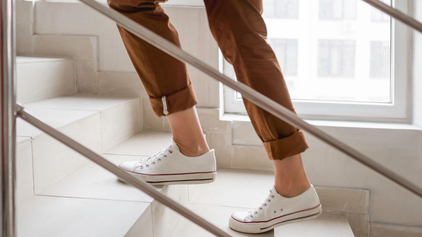 Frau in weißen Turnschuhen und Khakihose geht nach oben in ihre Wohnung.