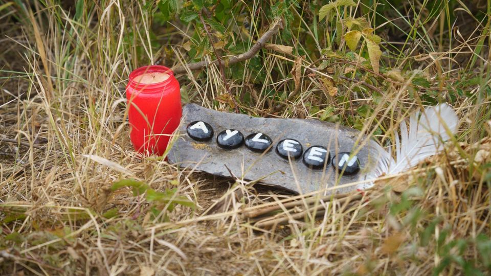 Neben einer Grabkerze liegt ein Stein mit aufgemaltem "Ayleen" im Gras