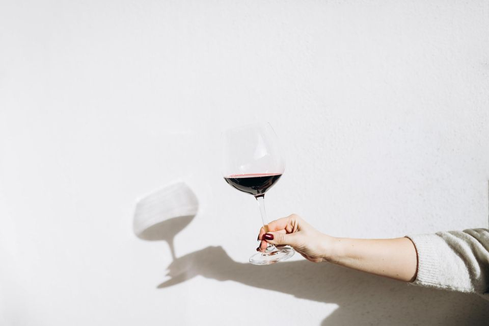 A woman holds a glass of red wine in his hand in front of a white wall