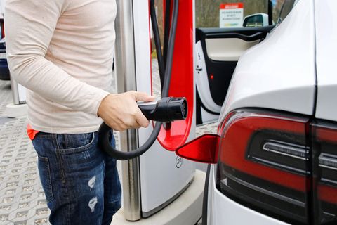 Eine Person hält einen Ladestecker neben einem Elektroauto in der Hand