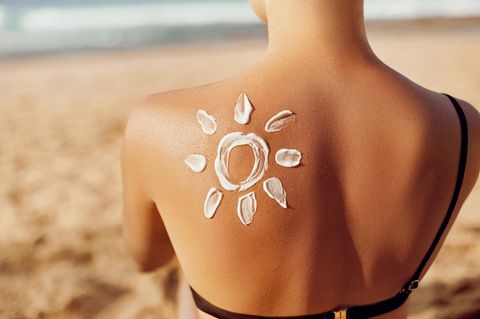 Auf dem Rücken einer Frau ist mit Creme eine Sonne aufgemalt.