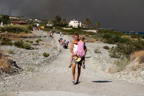 Ein Mann trägt auf der Ulraubsinsel Rhodos ein Kind, als sie ein Waldbrandgebiet verlassen