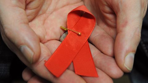 Ein mit dem HI-Virus infizierter Mann hält eine rote Schleife als Symbol der Solidarität mit HIV-Positiven und Aids-Kranken