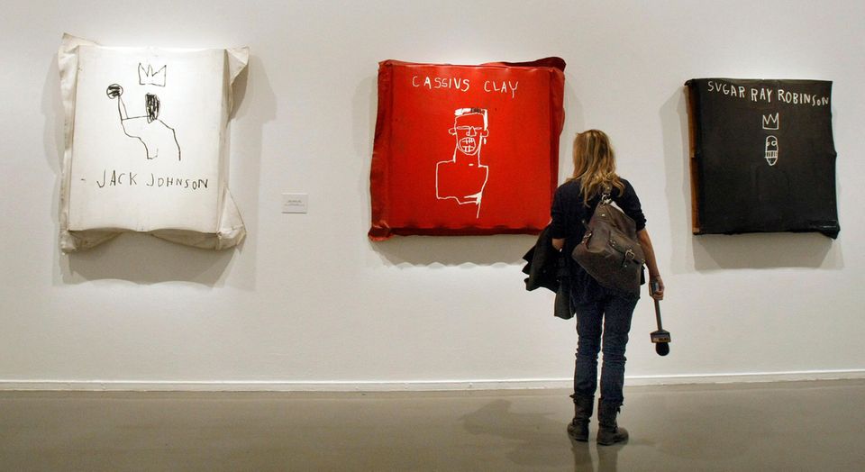 A woman stands in front of three works by the artist Jean-Michel Basquiat. Dua Lipa has a work by the artist.