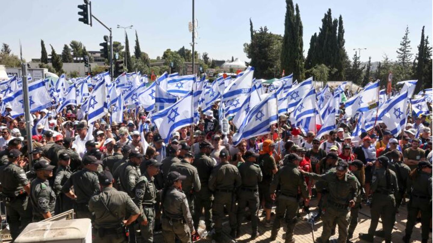 Israelische Sicherheitskräfte stehen Wache, während Demonstranten die Nationalflagge
