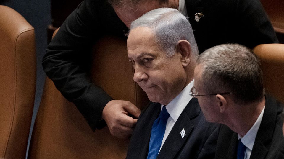 Israels Premierminister Benjamin Netanjahu sitzt in der Knesset, während ein Mann sich zum Gespräch über ihn beugt