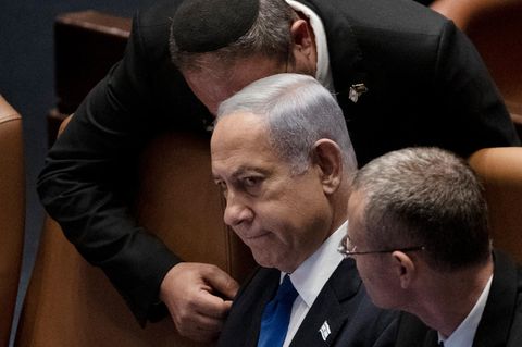 Israels Premierminister Benjamin Netanjahu sitzt in der Knesset, während ein Mann sich zum Gespräch über ihn beugt
