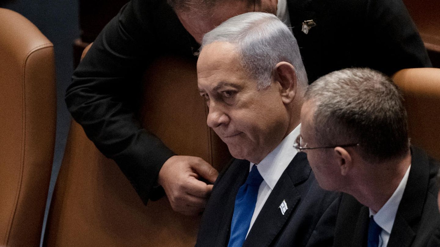 Israels Premierminister Benjamin Netanjahu sitzt in der Knesset, während ein Mann sich zum Gespräch über ihn beugt