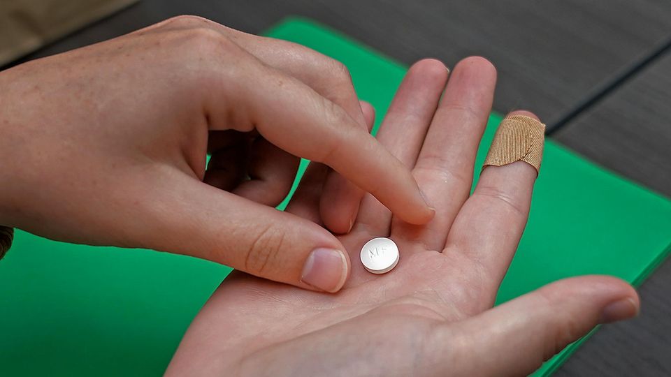 Eine weiße Abtreibungspille liegt auf der rechten Hand einer Frau, während die linke danach greift