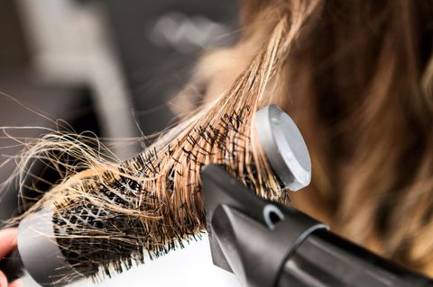 Lange blonde Haare sind um eine Rundbürste gewickelt und werden geföhnt.