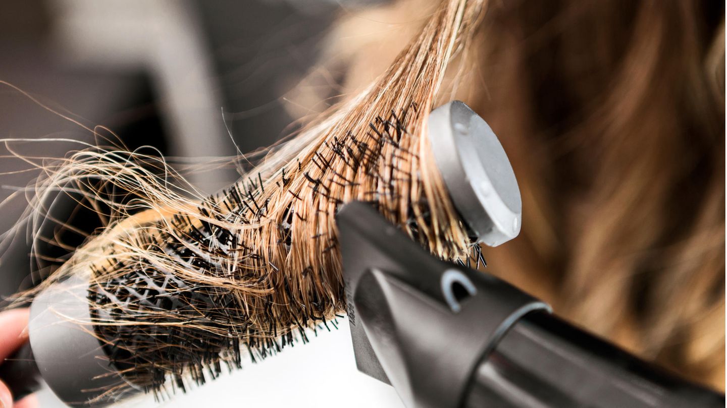 Lange blonde Haare sind um eine Rundbürste gewickelt und werden geföhnt.