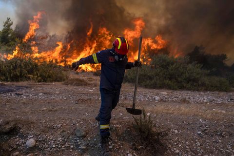 Ein Feuerwehrmann entfernt sich von Flammen eines Feuers auf Rhodos