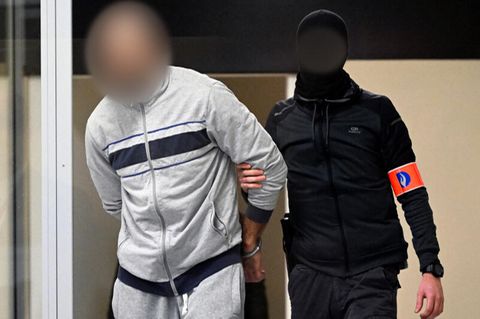 Ein vermummter Spezialpolizist bringt einen der Angeklagten in den Glaskasten in den Verhandlungssaal (Archivbild)