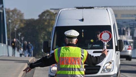 Ein Polizist mit Warnweste und Kelle winkt einen weißen Transporter für eine Kontrolle aus dem Verkehr in Brandenburg