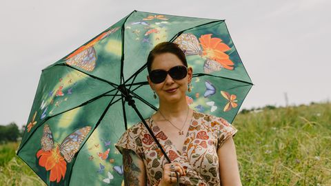 Frau im Blumenkleid mit Sonnenschirm und Sonnenbrille