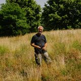 Mann im schwarzen T-Shirt steht vor Wiese