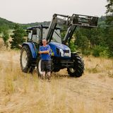 Mann mit blauem T-Shirt und dunkelgrauer Hose steht vor blauem Traktor