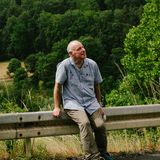 Mann sitzt auf Leitplanke an kleiner steiler Straße