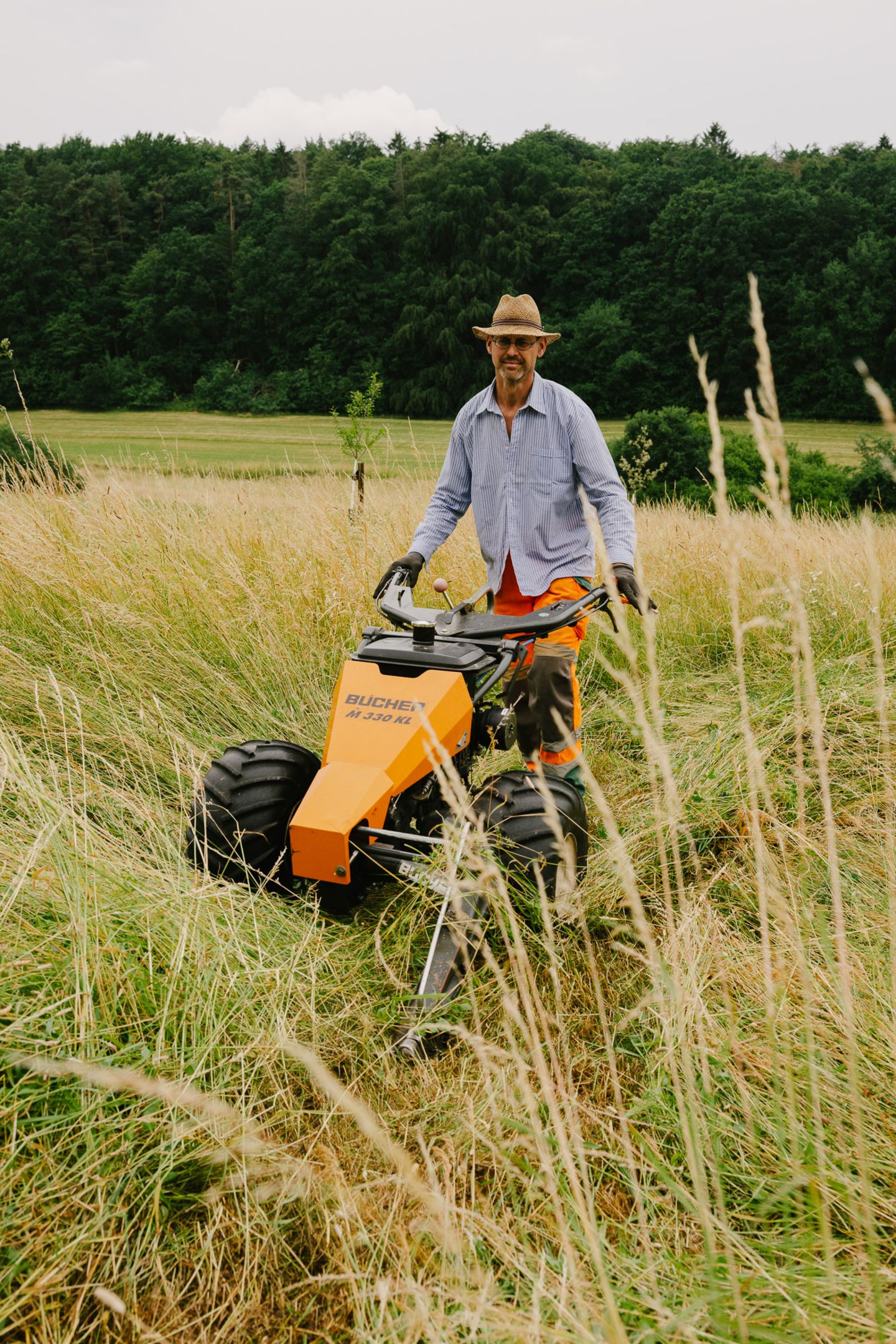 Mann mit orangefarbener Arbeitshose und hellbeigem Hemd und Sonnenhut