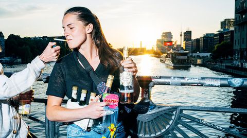 Eine junge Frau lässt sich Zigarette anzünden und steht auf einer Brücke mit Wein und Bier