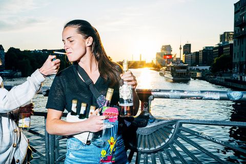 Eine junge Frau lässt sich Zigarette anzünden und steht auf einer Brücke mit Wein und Bier