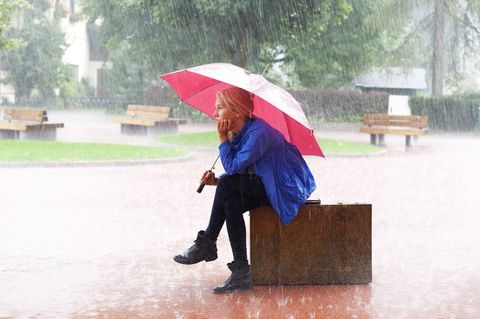 Frau sitzt mit Regenschirm im Regen