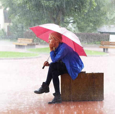 Frau sitzt mit Regenschirm im Regen