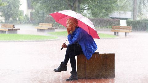 Frau sitzt mit Regenschirm im Regen