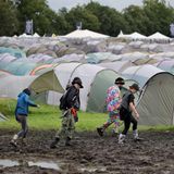 Besucher gehen an Zelten vorbei durch den Schlamm in Wacken