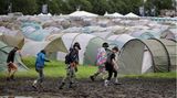 Besucher gehen an Zelten vorbei durch den Schlamm in Wacken