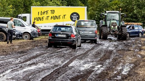 Ein Traktor zieht ein Auto zu einem Parkplatz auf dem schlammigen Wacken-Festivalgelände.