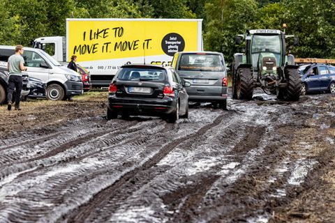 Ein Traktor zieht ein Auto zu einem Parkplatz auf dem schlammigen Wacken-Festivalgelände.