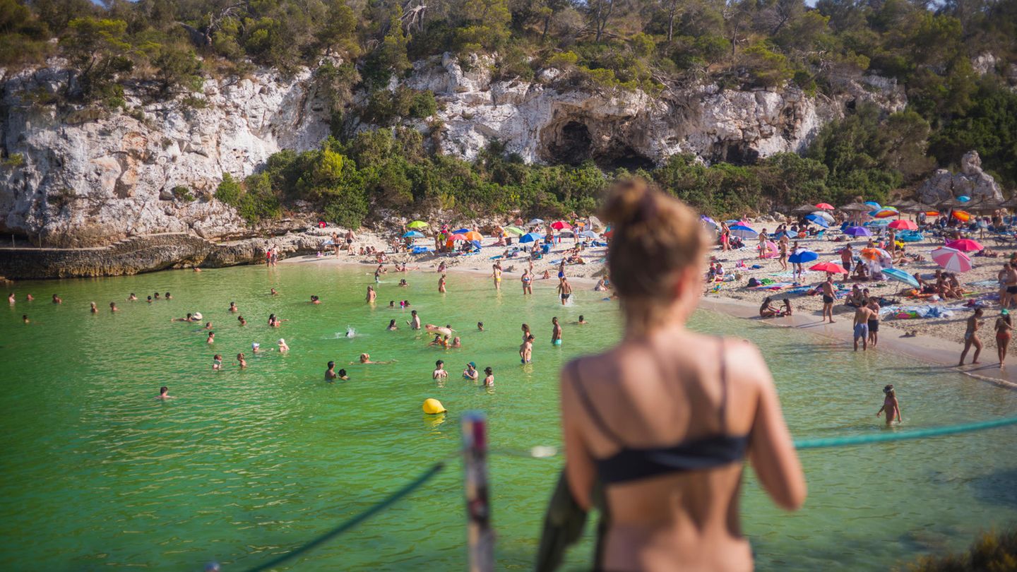 Eine Frau blickt auf den vollen Strand Cala Llombards auf Mallorca