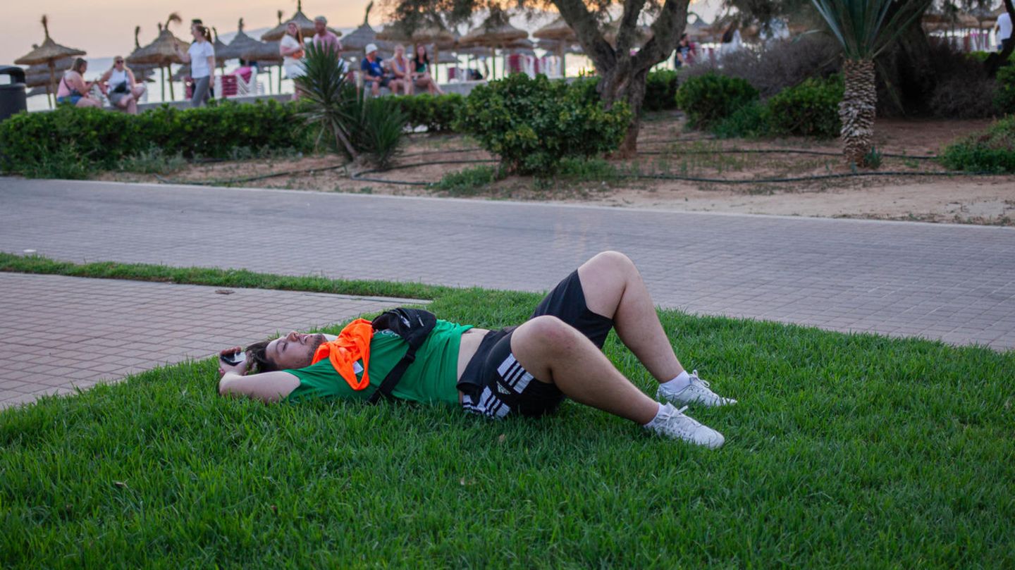 Ein betrunkener Partytourist liegt auf der Wiese am Strand von Mallorca