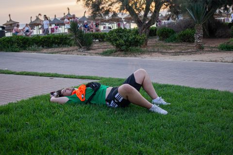 Ein betrunkener Partytourist liegt auf der Wiese am Strand von Mallorca