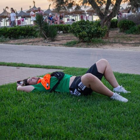 Ein betrunkener Partytourist liegt auf der Wiese am Strand von Mallorca