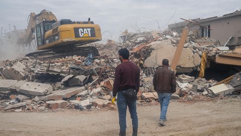 Menschen in Hatay sehen dabei zu, wie ein Bagger die Trümmer wegräumt