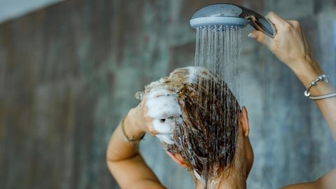 Eine Frau wäscht sich die Haare unter der Dusche.
