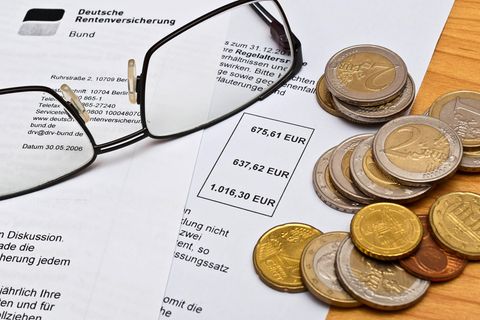 Rentenbescheid der Deutschen Rentenversicherung, auf dem eine Lesebrille und einige Euro-Münzen liegen