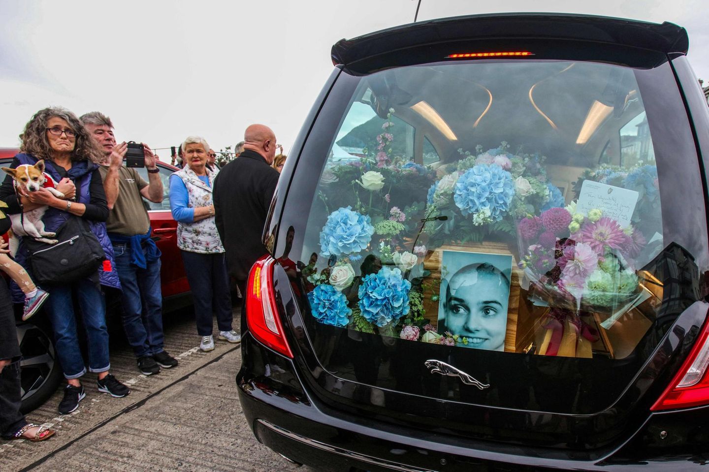 Der Kofferraum ist ausgeschmückt mit Blumen und Gestecken. Dazu erinnert ein Foto an die irische Sängerin, die 1990 mit dem Song "Nothing Compares 2 U" berühmt wurde. Das Stück war fünf Jahre zuvor von Prince komponiert worden, die von ihm protegierte Band The Family hatte es veröffentlicht. Erst Sinéad O'Connor verhalf dem Song zu Weltruhm - und der Song umgekehrt ihr. 