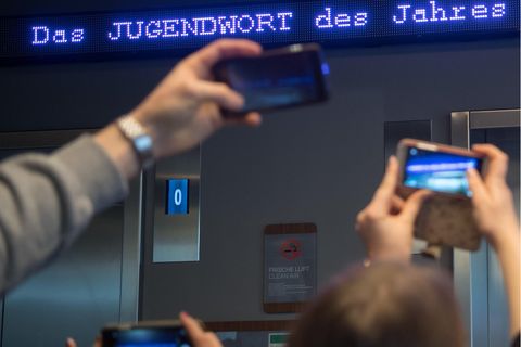 Auf einem Laufband erscheint "Jugendwort des Jahres" über den digitalen Newsticker eines Hotel.