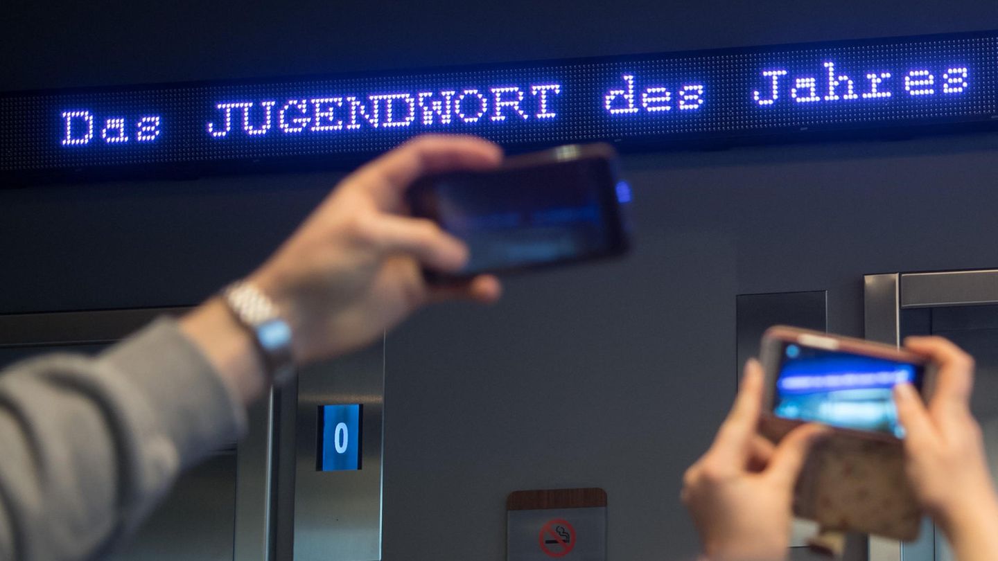 Auf einem Laufband erscheint "Jugendwort des Jahres" über den digitalen Newsticker eines Hotel.