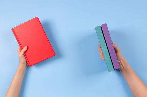 Hände halten drei Bücher vor blauem Hintergrund